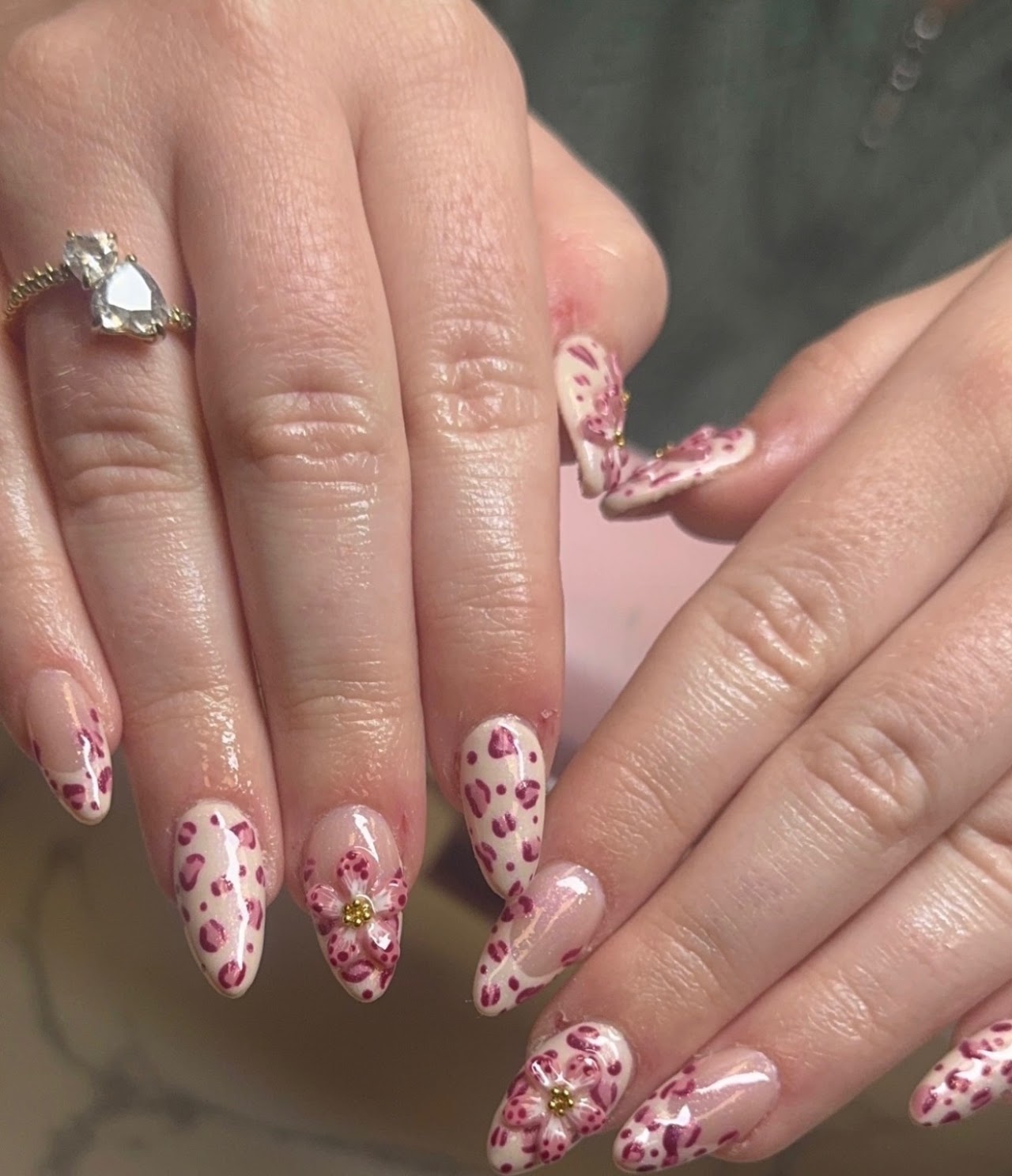 Elegant acrylic nail extensions with a modern teal and gold design. The nails are perfectly shaped and polished, reflecting a sophisticated aesthetic. The background consists of soft, blurred spa elements like flowers and marble textures, maintaining a serene and premium radiance color palette of pink and teal tones.